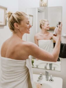 Woman in bathroom applying skin care spray to her face. For people with dermal fillers Hawaii patients can apply home skin care treatment to extend the effects of their fillers.