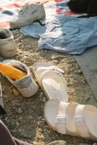 Shoes and sunscreen on the sand at the beach. Applying sunscreen is important to avoid skin cancer and melasma by Honolulu visitors and residents.