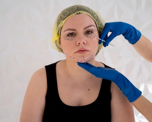 Hawaii plastic surgeon wearing blue gloves evaluates a patient's jawline prior to facial fat grafting.